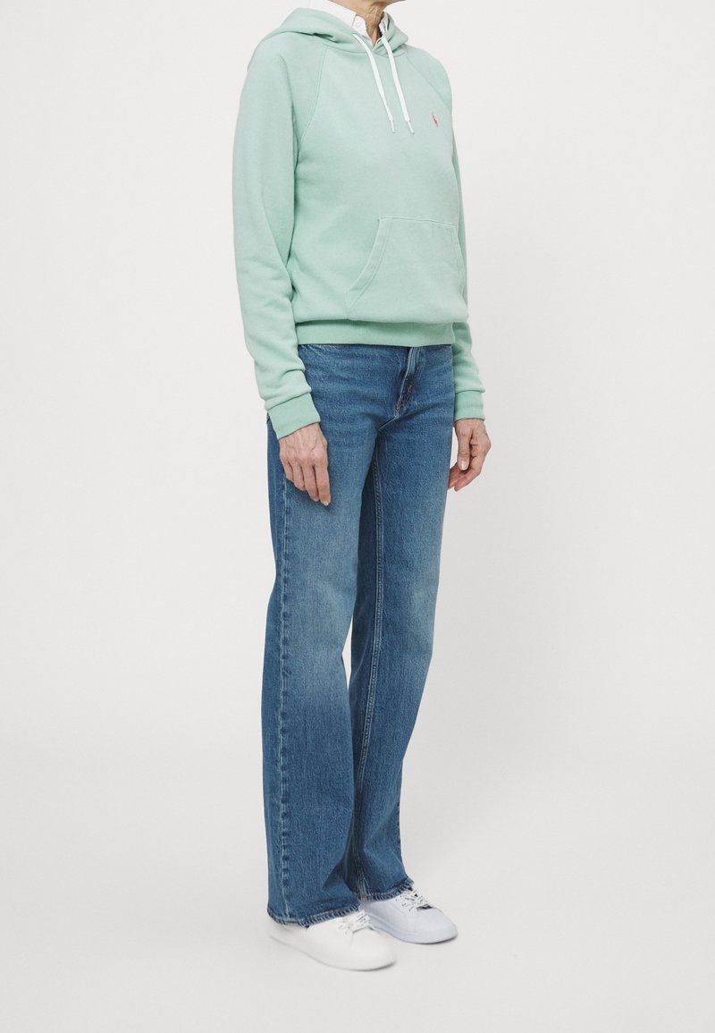 Mint green hoodie with front pocket, white drawstrings, paired with light blue straight-leg jeans and white sneakers.