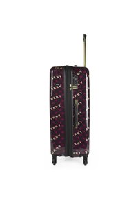 Maleta rígida morada con acabado brillante, herrajes dorados, cremallera negra y patrón repetido del logo de DKNY; incluye un asa retráctil y ruedas.