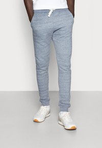 Pantalones de chándal texturizados de color azul claro con cintura ajustable y piernas acampanadas, combinados con zapatillas deportivas blancas con acentos en naranja.