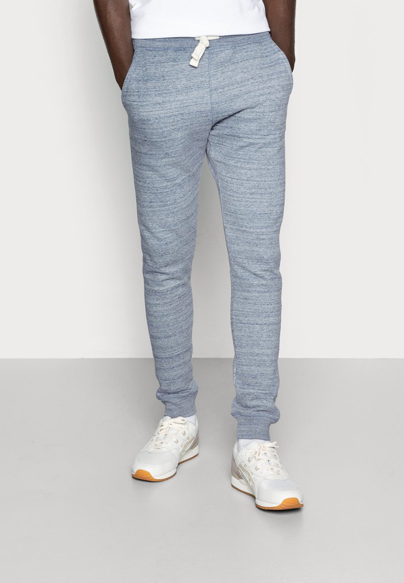 Pantalones de chándal texturizados de color azul claro con cintura ajustable y piernas acampanadas, combinados con zapatillas deportivas blancas con acentos en naranja.