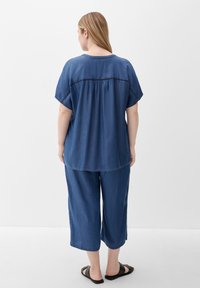 Blue denim top with short sleeves, gathered detail at the back, paired with loose-fitting blue denim culottes and black sandals.