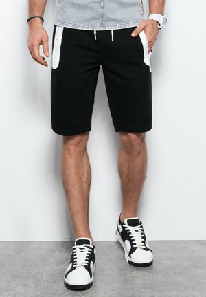 Pantaloni sportivi neri con tasche accentate bianche, vita regolabile con stringa e una vestibilità comoda, abbinati a scarpe da ginnastica nero e bianco.