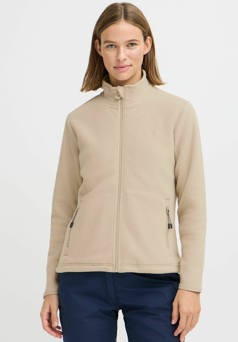 Beige fleece-takki, jossa on vetoketju edessä, korkea kaulus ja kaksi sivuvetoketjullista taskua. Sileä pinta, jossa on hienovarainen brändäys rinnassa.