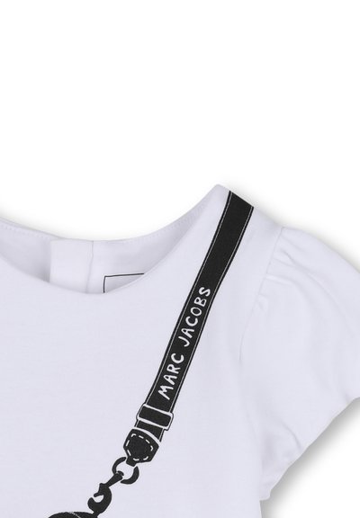 T-shirt blanc à manches ballon, avec un design de bretelle noire comportant le texte "MARC JACOBS" et un graphique de chaîne. Matière en coton doux.