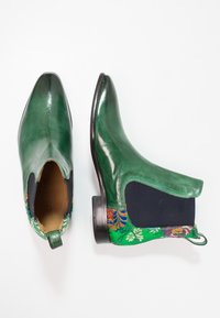 Botas de tobillo verde de cuero con punta afilada y paneles laterales elásticos en color marino, que presentan un patrón de flores bordadas en el talón.