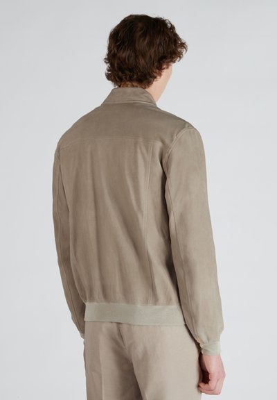 Giacca in suede beige con polsini e orlo a costine. Presenta un colletto e una superficie testurizzata per un aspetto uniforme. La vista posteriore mostra i dettagli delle cuciture.