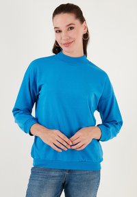 Sudadera de color azul brillante con cuello alto, mangas largas y puños y dobladillo acanalados. Textura de tela suave y ajuste holgado.
