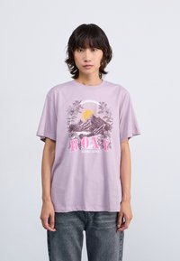 Light purple cotton t-shirt featuring a graphic design with mountains, sun, and the "ROXY" logo in pink. Relaxed fit and short sleeves.