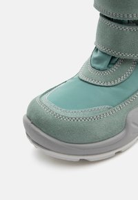 Bota turquesa con acabado de ante, que presenta acentos y costuras en gris, correas de Velcro y una suela texturizada para mayor agarre.
