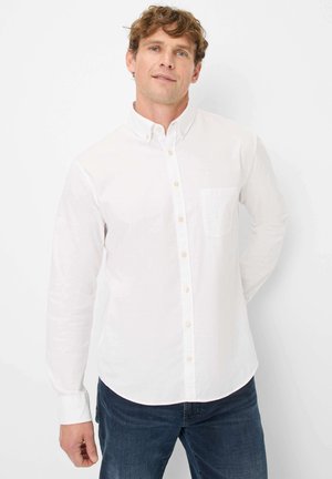 Chemise blanche à manches longues en coton, avec une poche poitrine et un col pointu. Associée à un jean bleu foncé.