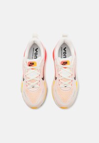Zapatillas de running con una parte superior de malla transpirable en blanco y degradado rosa, acentuadas por un swoosh negro, un talón amarillo y una suela texturizada.