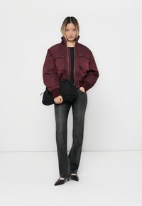 Burgundy bomber jacket with two chest pockets, black long-sleeve top, dark gray flared pants, and black pointed-toe shoes.
