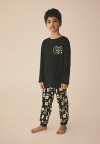 Langärmliges schwarzes Baumwollhemd mit einem goldenen Grafik und passenden schwarzen Hosen mit einem bedruckten Muster aus Sternen und Monden.
