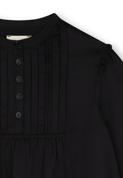 Zwarte blouse met een ronde halslijn, verticale plooien, knoopsluiting vooraan met zes zwarte knopen, en subtiele ruches aan de mouwen. Zachte stofstructuur.