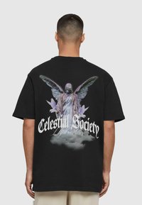 Sort t-shirt med et stort grafisk tryk af en figur med vinger og teksten "Himlens Samfund Loyal Alliancer" i hvide og lilla nuancer.