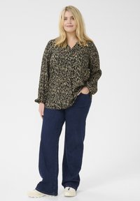 Blusa a maniche lunghe e con bottoni in stampa animale nera e verde, abbinata a jeans a gamba larga blu scuro e sneakers chiare.