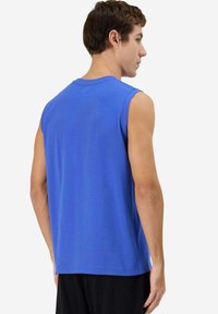 T-shirt senza maniche in cotone blu con scollatura rotonda e vestibilità morbida, caratterizzata da una texture liscia e un orlo dritto. Sono visibili pantaloni corti neri.