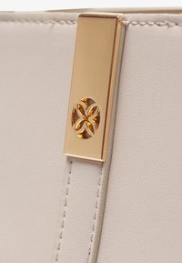 White faux leather material with a smooth texture, featuring a gold-tone metal accent with a decorative cut-out floral design.