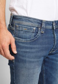 Jeans i denim i en medelblå tvätt, med rak passform, fem fickor, silverfärgad hårdvara och kontrasterande gula sömdetaljer.