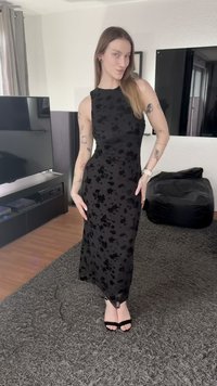 Vestido longo preto com estampado floral, silhueta ajustada, design sem mangas e brilho subtil. Combinado com sandálias pretas de tiras.