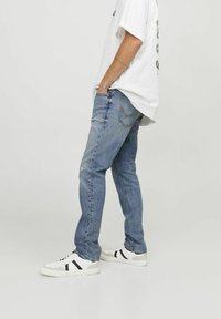 Jeans de mezclilla azul claro con un diseño de pierna recta, que presentan costuras en contraste y detalles de desgaste sutiles. Combinados con zapatillas blancas.
