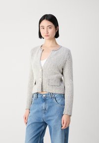 Grijze cardigan met een houndstoothpatroon, een cropped ontwerp, ronde hals en twee voorzakken. Knopen zijn gemaakt van een lichte materiaal.