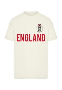 Kremo spalvos marškinėliai su raudonu "ENGLAND" spaudiniu ir juodu bei raudonu skydo logotipu viršuje kairėje krūtinės pusėje. Trumpomis rankovėmis, pagaminti iš medvilnės.
