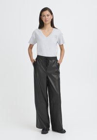 Maglietta grigia a scollo a V e pantaloni larghi in ecopelle nera con cintura elastica, caratterizzati da tasche laterali e una texture liscia.