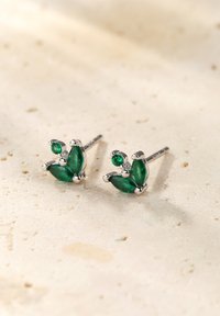 Pendientes de stud de gema verde con acentos de plata, presentando formas parecidas a hojas en varios tamaños y un acabado pulido sobre una superficie de piedra clara.