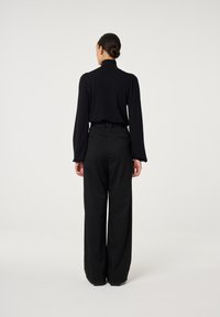 Schwarzes Oberteil mit hohem Kragen und langen Ärmeln, kombiniert mit weiten schwarzen Hosen. Glatte Stoffstruktur mit tailliertem Design für einen eleganten Look.