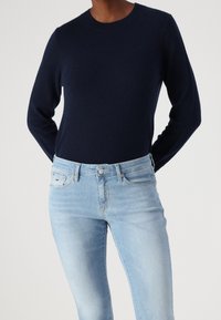 Persona que lleva un suéter ajustado de color azul marino oscuro metido dentro de unos jeans de mezclilla azul claro con estilo clásico de cinco bolsillos y cierre de botón.