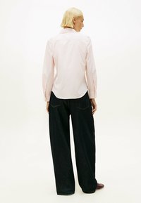 Camisa de rayas rosas con botones, mangas largas, puños angulados y dobladillo curvado, combinada con vaqueros de mezclilla oscuros de pierna ancha.