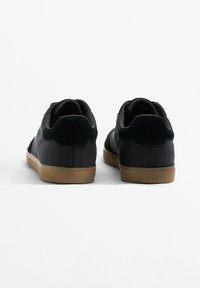 Black sporty shoes with a textured rubber sole, featuring a suede accent at the heel and a sleek profile without visible laces.