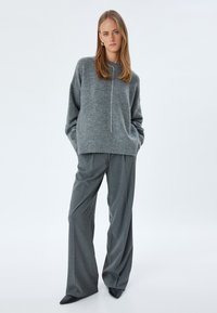 Grijze gebreide trui met een ronde hals en subtiele witte stiksels, gecombineerd met losse grijze broek met een structuurstof en wijde pijpen.