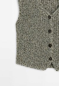 Gilet lavorato a maglia in filato nero e crema con un motivo testurizzato, caratterizzato da cinque bottoni tondi marroni sul davanti. Senza maniche, design a scollatura a V.