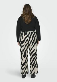 Zwarte top met lange mouwen gecombineerd met brede, zwart-wit zebraprint broek. De stof lijkt gestructureerd met een elastische tailleband.