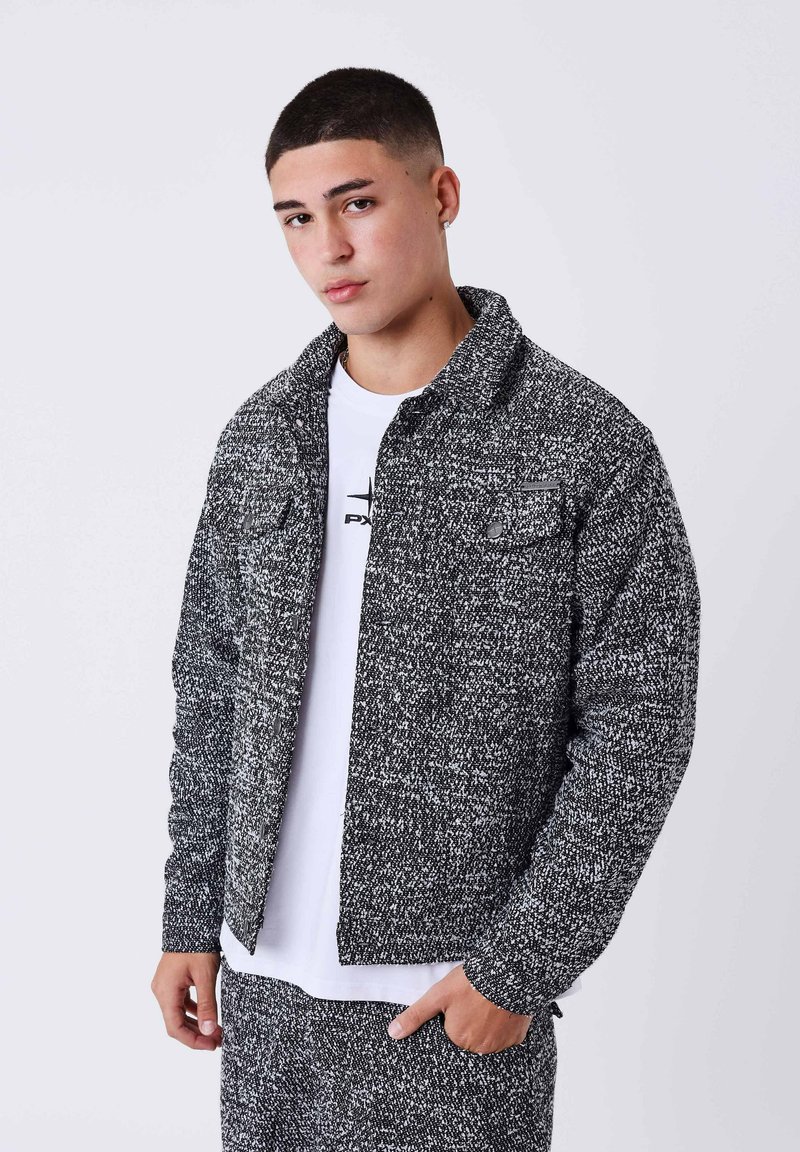Giovane uomo con capelli corti che indossa un giaccone texturizzato bianco e nero e pantaloni abbinati, con una t-shirt grafica bianca sotto.