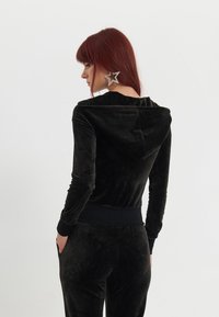 Zwarte fluwelen hoodie met een ontspannen pasvorm, voorzien van een capuchon en geribde mouwen. Gladde textuur, minimalistisch ontwerp, geen zichtbare patronen of accenten.