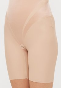 Nude formeringsshorts laget av glatt, elastisk materiale. Har en tettsittende design med midt-inn til låret lengde og sømløse kanter for komfort.