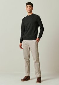 Mørkegrå strikket sweater, lys beige bukser og brune lædersko. Glat struktur, rund halsudskæring og standard pasform.