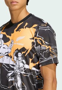 Czarny i pomarańczowy koszulka sportowa z graficznymi ilustracjami, krótkimi rękawami i okrągłym dekoldem; materiał wydaje się gładki i lekki.