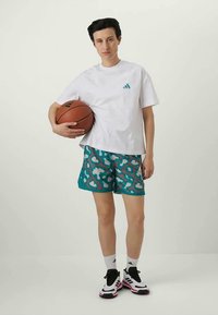 Camiseta blanca de manga corta con el logo de Adidas en color turquesa, pantalones cortos estampados en turquesa y zapatillas deportivas negras/rosas; sosteniendo un balón de baloncesto.