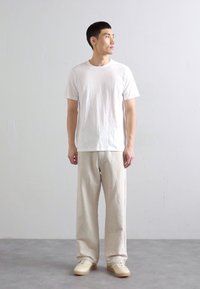 T-shirt bianco a maniche corte abbinato a pantaloni beige larghi e sneakers di colore chiaro. Tessuto liscio con una vestibilità rilassata, design minimalista.