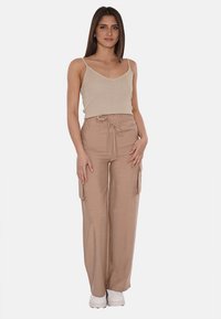 Top in tessuto a costine beige con spalline sottili, abbinato a pantaloni cargo beige a gamba larga con tasche laterali e vita regolabile con cordino.