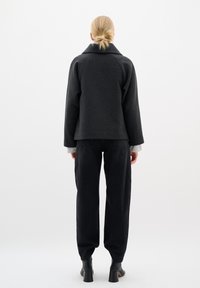 Graue Wollmischungjacke mit großem Kragen, abgerundeten Schultern und lockerer Passform, kombiniert mit schwarzen, hochtaillierten Hosen und geschnürten Stiefeletten.