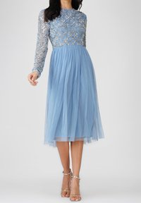 Vestido midi azul claro con mangas largas de tul, busto adornado con intrincados bordados en plata y falda de tul fluida.