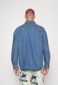 Camicia in denim, blu medio, maniche lunghe, polsini con bottoni, dettaglio cucitura sulla yoke posteriore, vestibilità rilassata, spacchi laterali all'orlo.