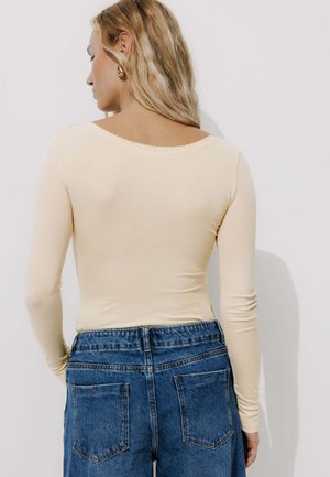 Haut à manches longues de couleur jaune clair avec un col rond, associé à un pantalon en denim bleu taille haute avec des poches arrière.