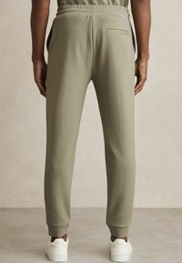 Pantalones de chándal verde oliva con corte recto, cinturilla elástica y bolsillos laterales, con un único bolsillo trasero. Tejido texturizado.