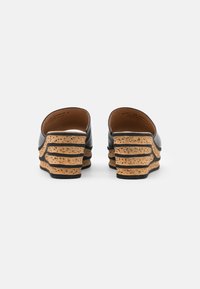 Mules à talons en cuir noir avec plateforme en liège. Présente un design à wedge en couches ondulées, un matériau texturé et un intérieur lisse.